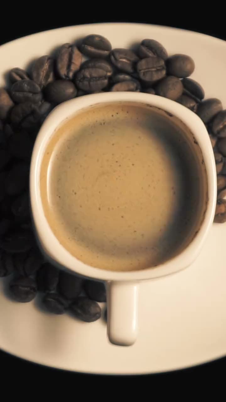 A cup of coffee on a saucer of coffee beans, seen from above.